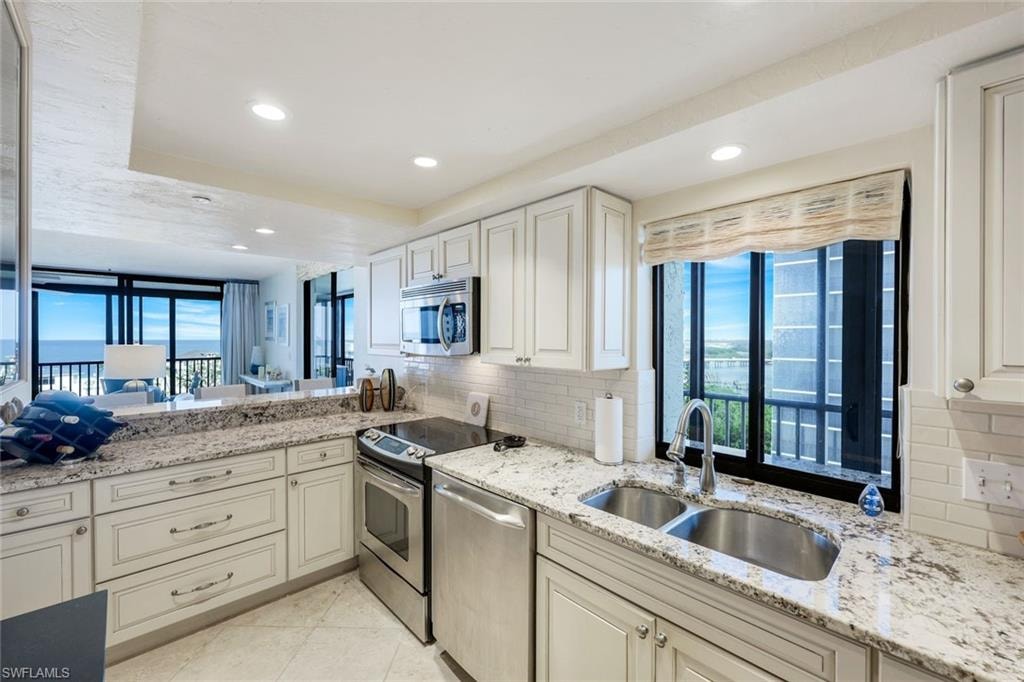 Kitchen featuring white shaker cabinetry, stainless steel appliances, a subway tile backsplash, and light-toned stone countertops