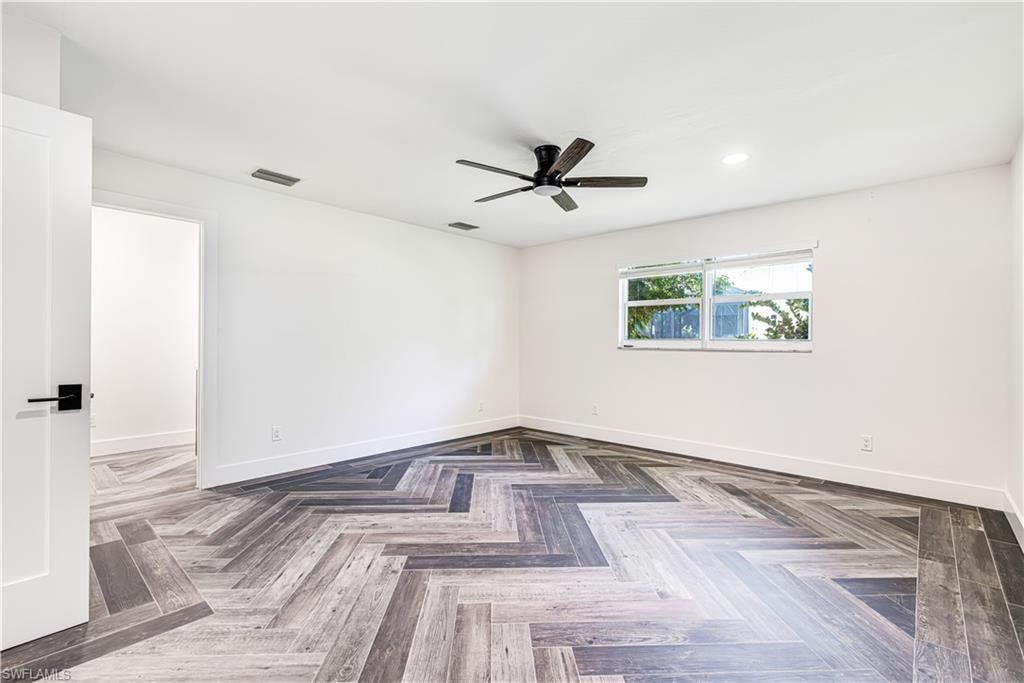 Spacious room with herringbone-patterned wood-finish flooring, white walls, and a contemporary black ceiling fan
