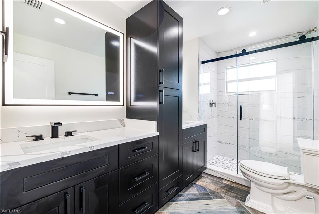 Nicely appointed bathroom featuring a dark wood-finish double vanity with white countertops, an illuminated mirror, a glass-enclosed shower with white tiled walls, and patterned floor tile