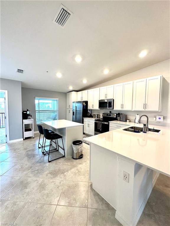 Kitchen with lofted ceiling, appliances with stainless steel finishes, white cabinets, sink, and a kitchen bar