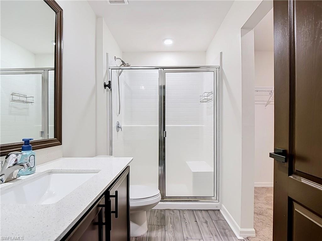 Bathroom featuring wood-finish flooring, a contemporary vanity with a white countertop and rectangular sink, a framed mirror, and a shower with sliding glass doors and white subway tile surround