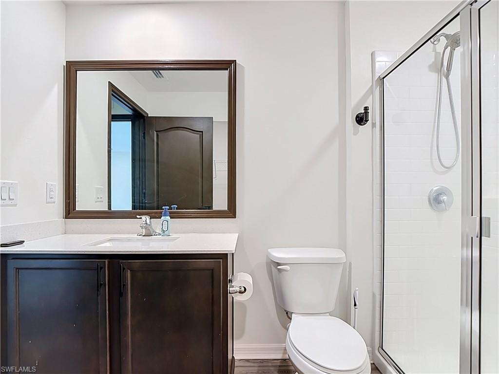 Bathroom featuring a dark wood-finish vanity with a white countertop and undermount sink, framed mirror, and a walk-in shower with subway tile surround and clear glass enclosure