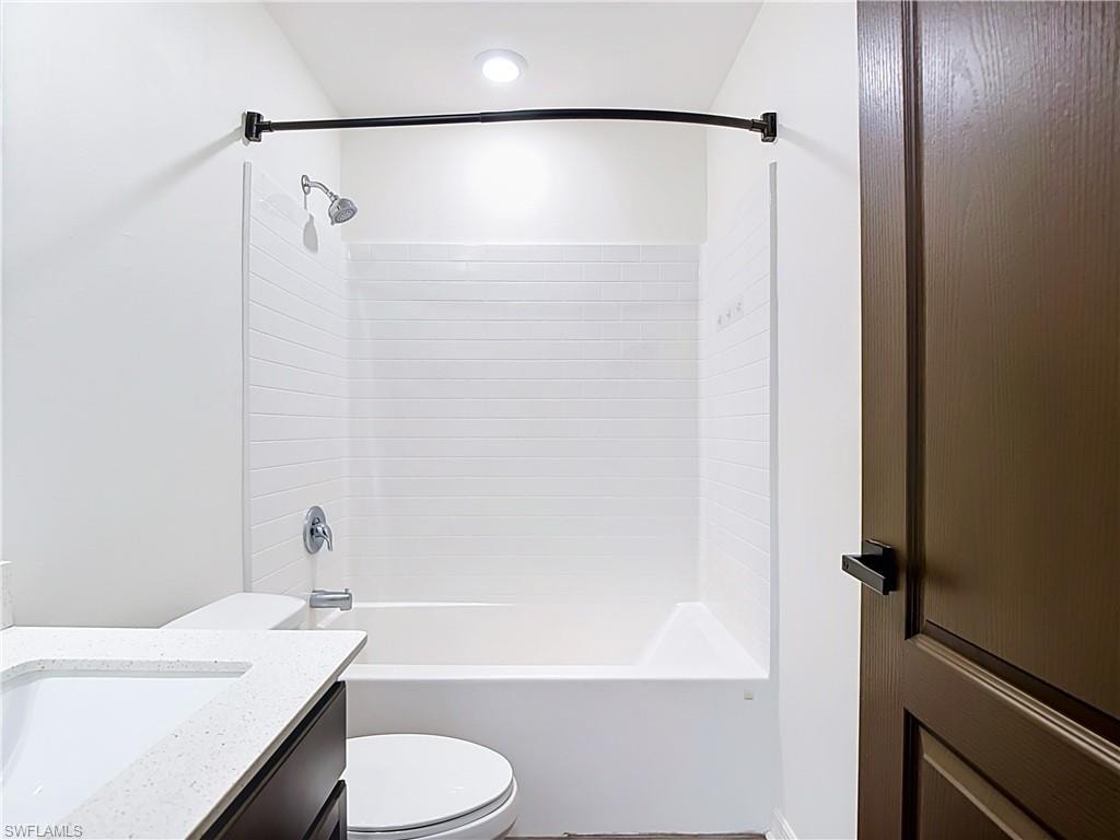 Bathroom featuring a white subway tile tub surround, chrome fixtures, a dark wood-finish vanity with a light-toned countertop, and a recessed ceiling light
