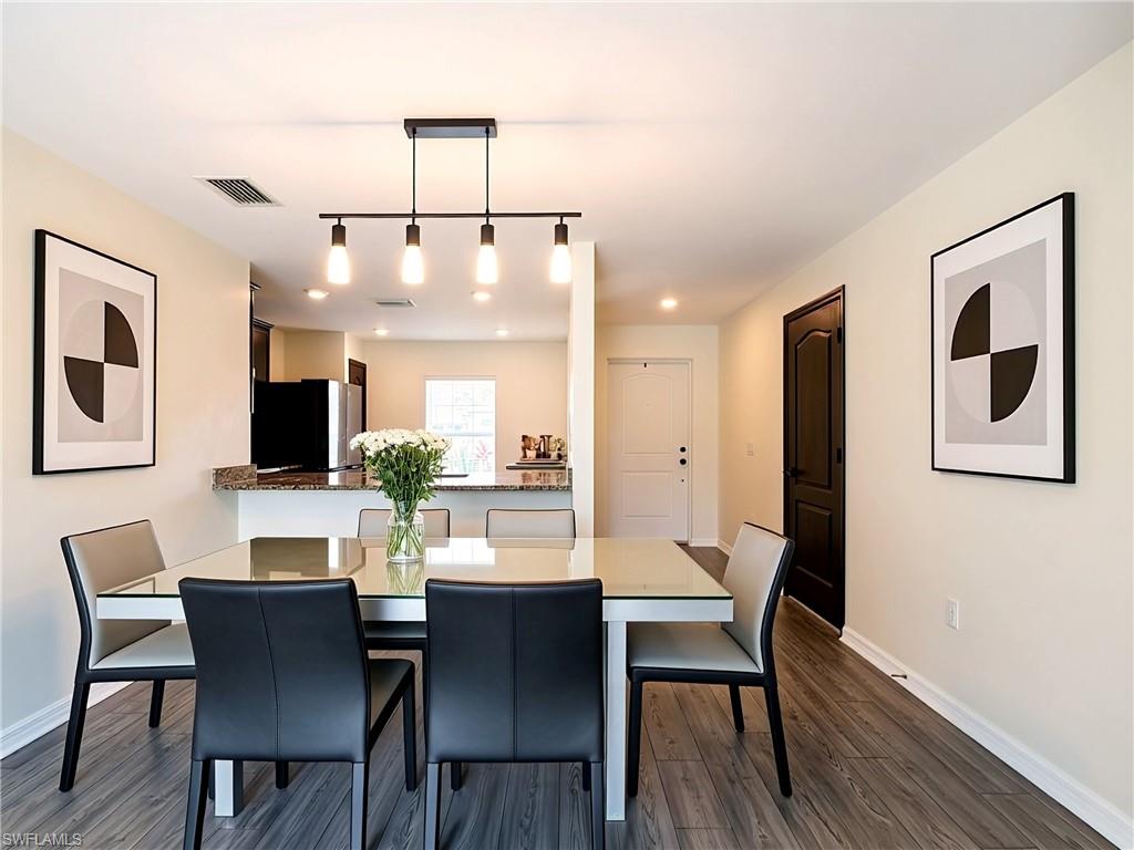 Dining area featuring wood-finish flooring, a modern linear chandelier, and a pass-through opening to the kitchen