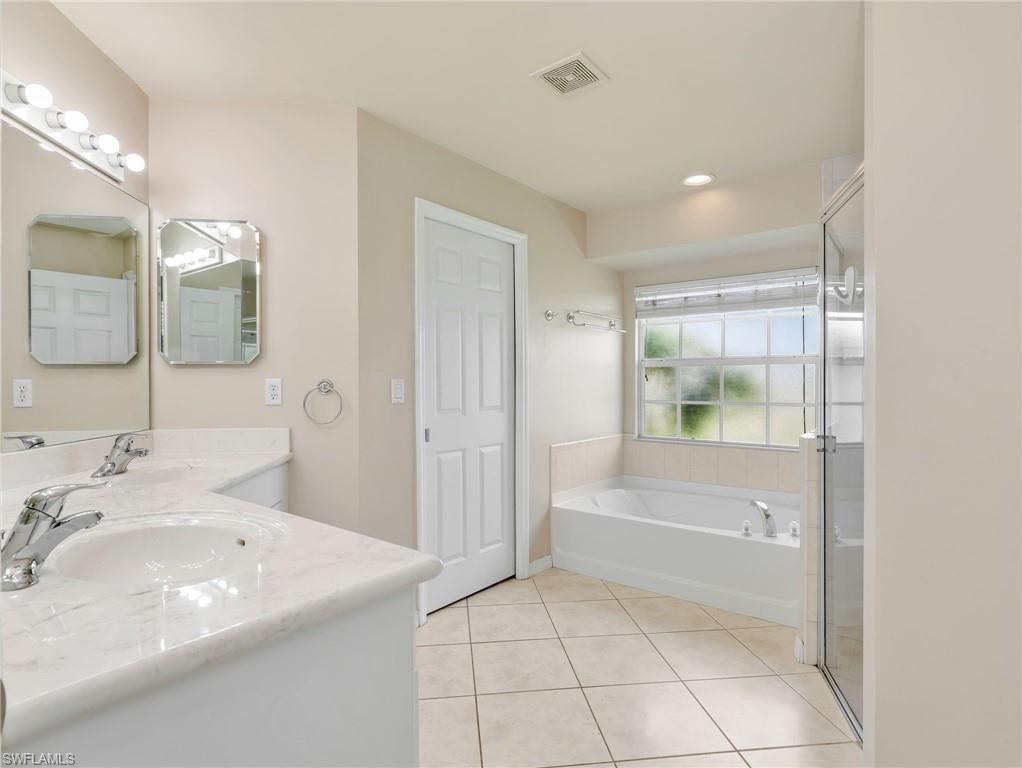 Primary Bathroom with White Cabinetry, Tile Flooring, Dual Sinks, Soaking Tub & Walk in Tile Shower with Glass Enclosure