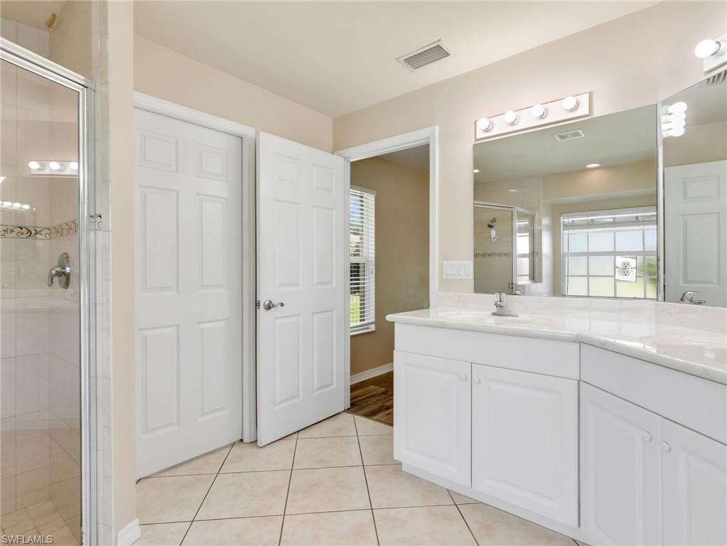 Primary Bathroom with White Cabinetry, Tile Flooring, Dual Sinks, & Walk in Tile Shower with Glass Enclosure