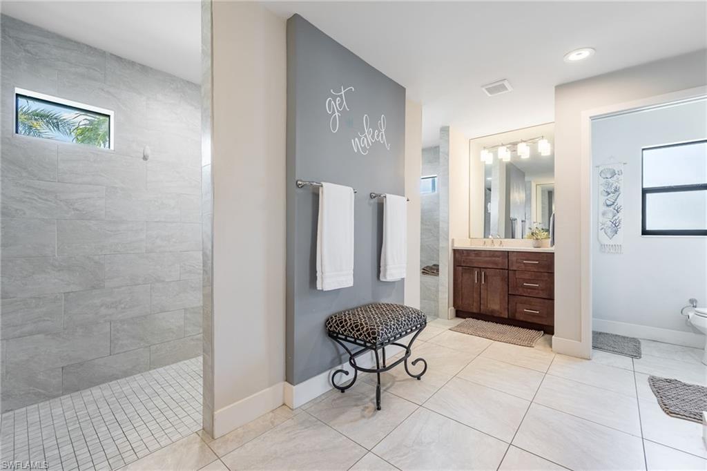 Bathroom featuring a walk-in shower with large format tile, a vanity with a dark wood-finish cabinet, a rectangular undermount sink, and a framed mirror with integrated lighting