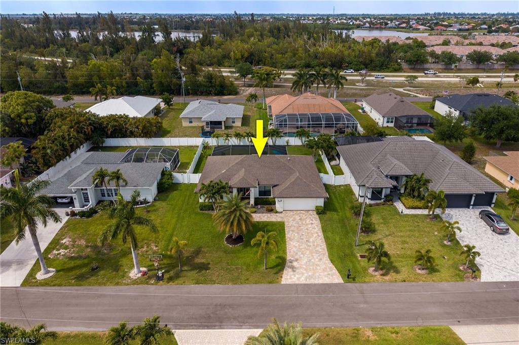 Single-story residence featuring a paved driveway, mature palm trees, and a screened-in pool enclosure