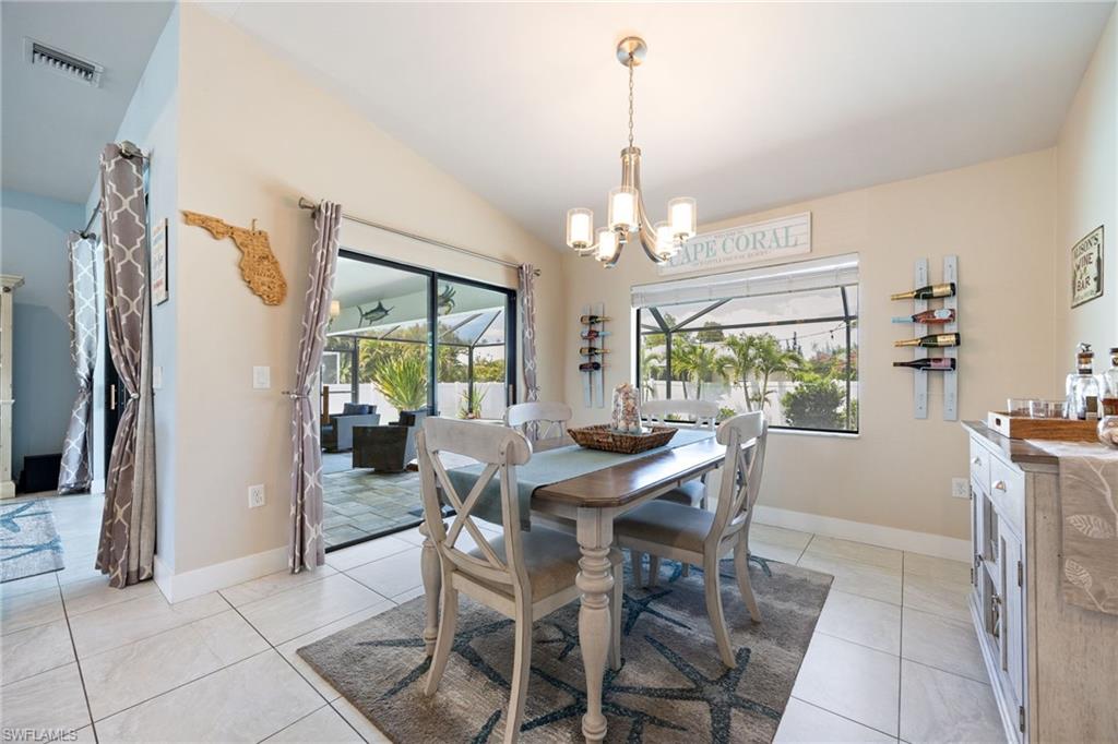 Vaulted ceiling dining area with tiled flooring, a contemporary chandelier, and sliding glass doors opening to an outdoor screened lanai