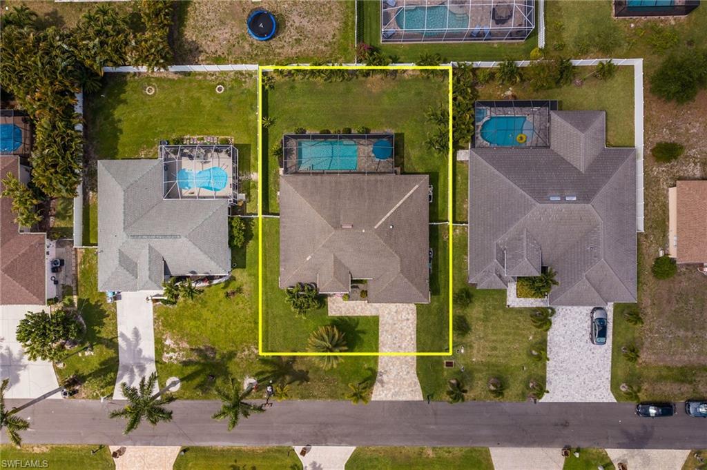 Property featuring a screened outdoor pool, a perimeter fence, a paved driveway, and mature landscaping