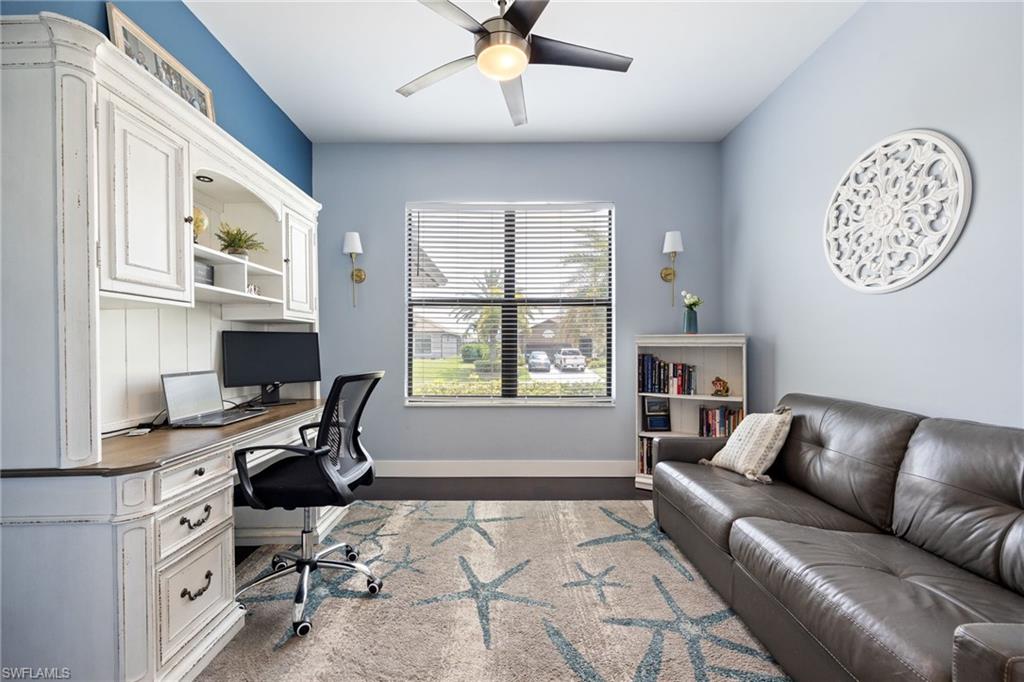 Dedicated workspace featuring a built-in hutch with storage, a large window, a ceiling fan with integrated lighting, and dark wood-finish flooring