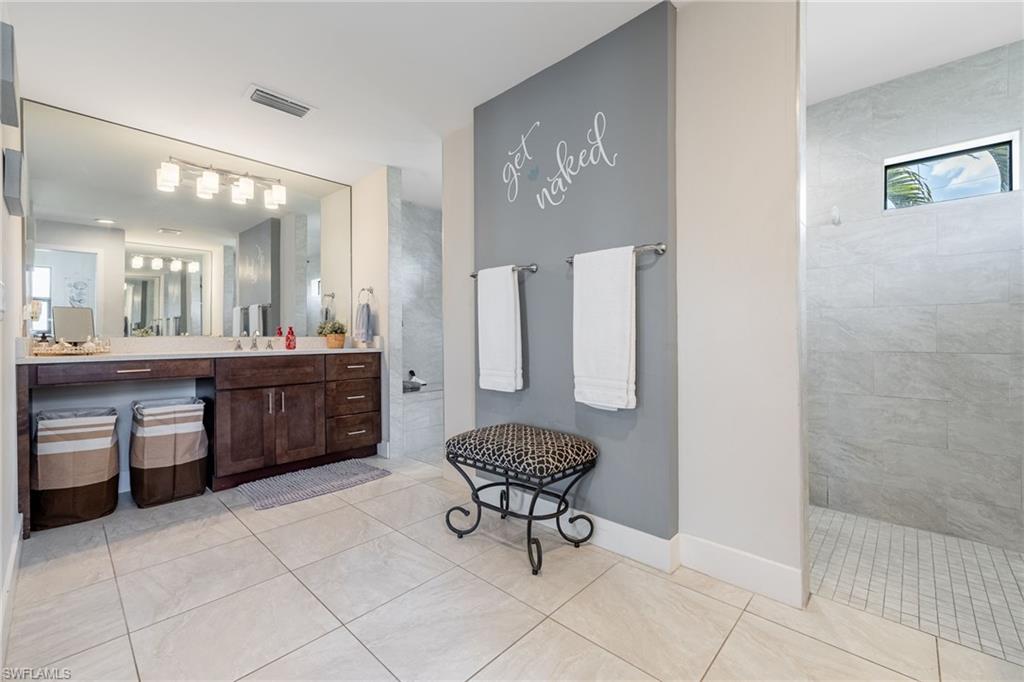 Spacious bathroom featuring large format floor tiles, an expansive vanity with double sinks, and a walk-in shower with a frosted transom window