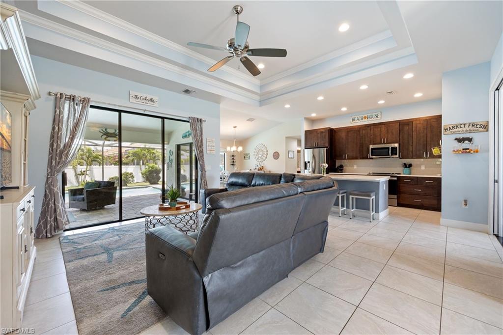 Open-concept living space featuring light tile flooring, a tray ceiling with recessed lighting, and a ceiling fan