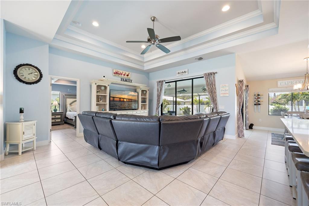Spacious living area featuring a tray ceiling with recessed lighting and a ceiling fan, large format tile flooring, and a sliding glass door offering abundant light