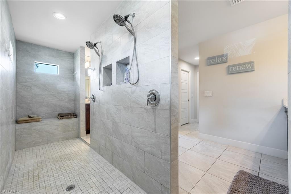 Spacious walk-in shower featuring light gray tile walls, a built-in bench, dual showerheads, and recessed wall niches