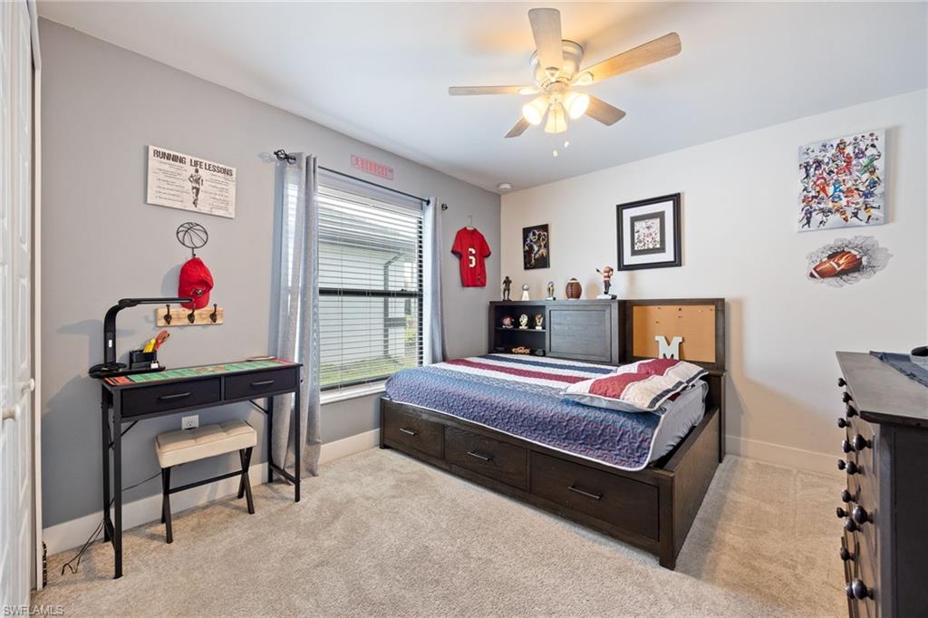 Neutral-toned bedroom featuring a ceiling fan with integrated lighting, a window with horizontal blinds, and plush carpeting