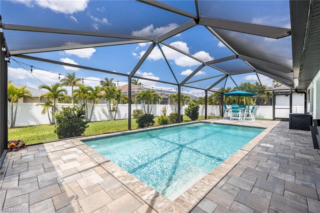 Screened-in outdoor pool area featuring a rectangular pool, paver decking, and a privacy fence