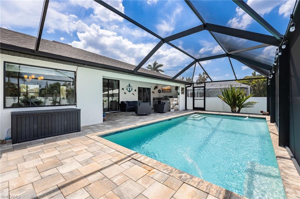 Screened-in swimming pool featuring a paver deck, built-in steps, and an outdoor living area