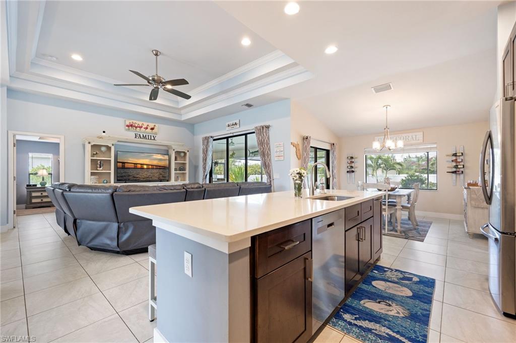 Open-concept living space featuring a central kitchen island with a light-toned countertop, stainless steel appliances, and dark wood-finish cabinetry