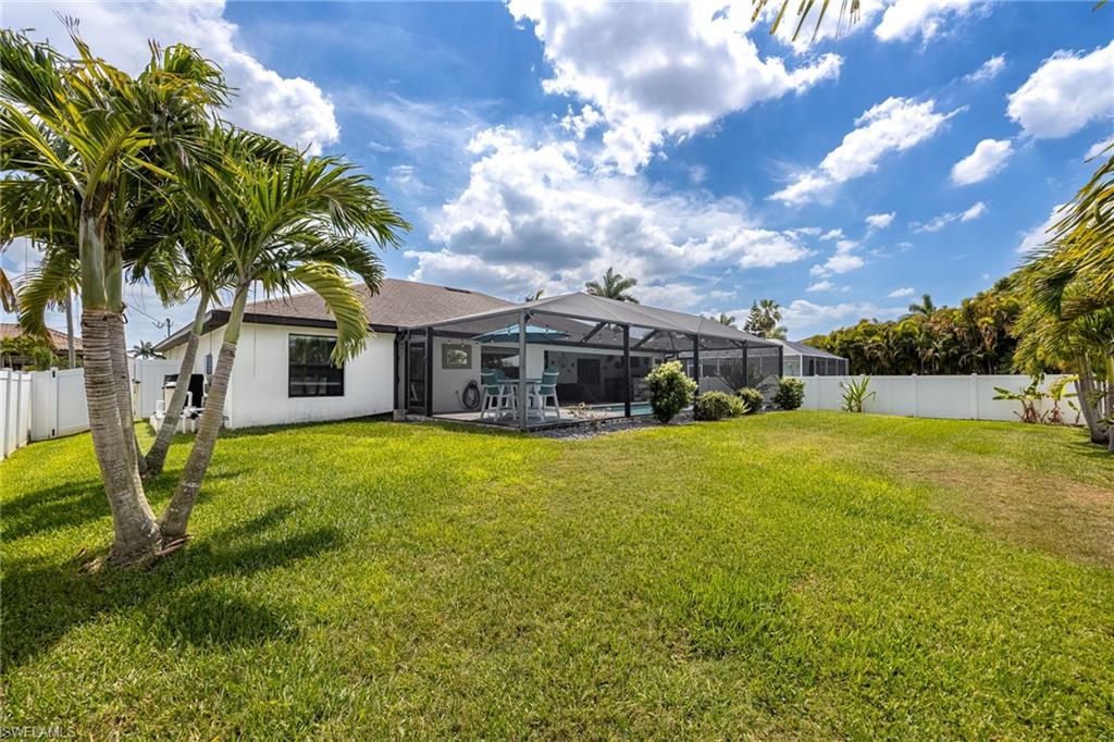 Expansive rear yard with manicured lawn, mature palm trees, and covered patio structure