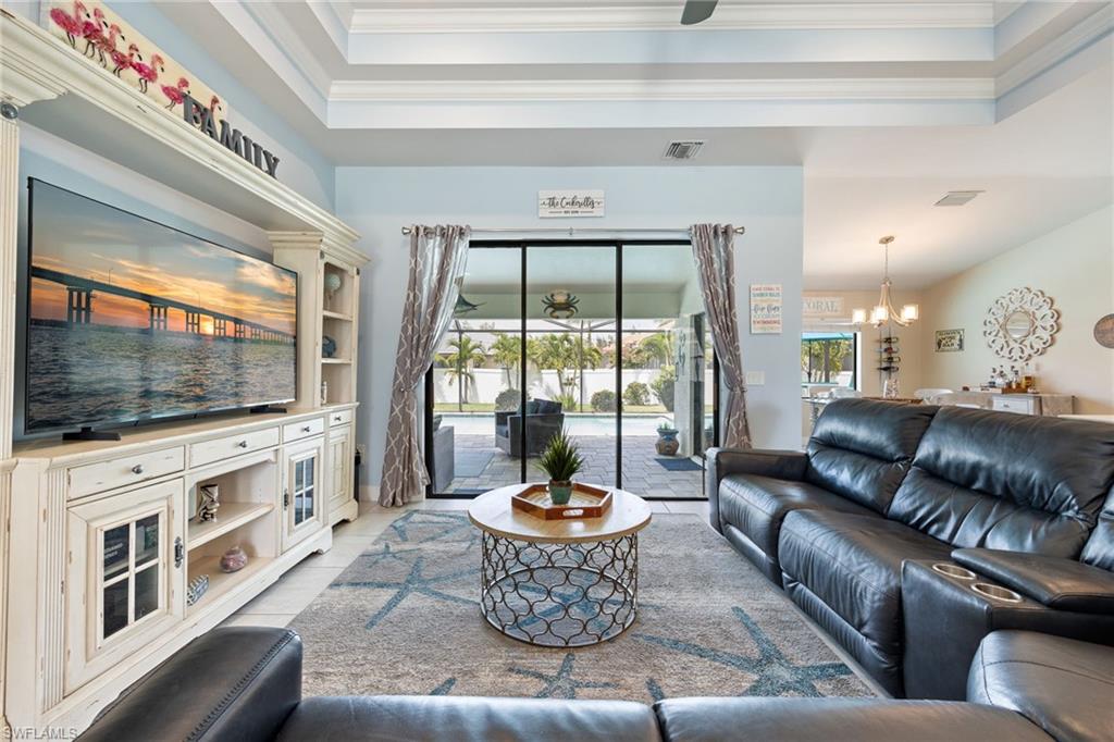 Living area featuring a coffered ceiling, tile flooring, and sliding glass doors opening to a paved patio with a swimming pool