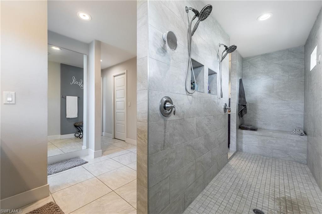 Spacious walk-in shower featuring dual shower heads, tiled walls, built-in shelving, and a tiled bench