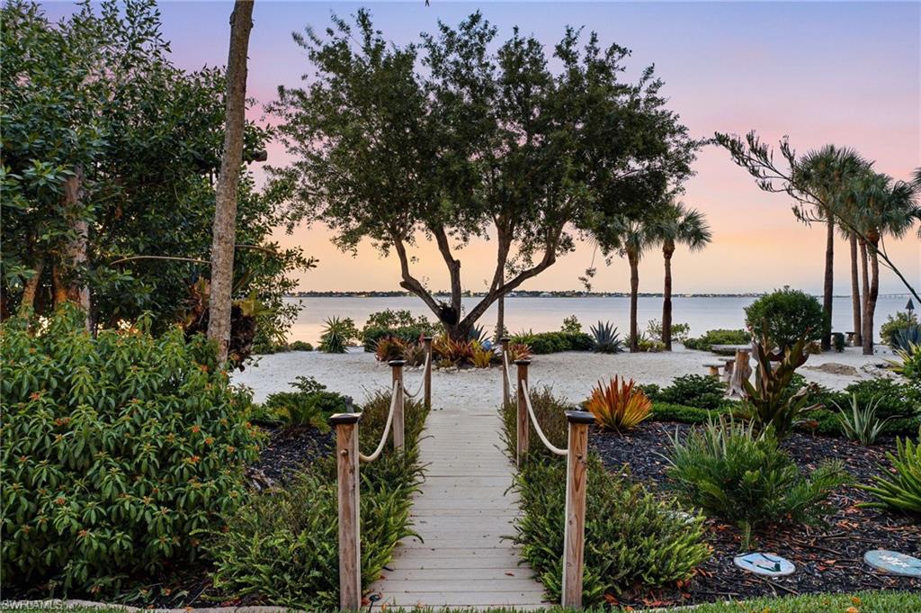 A beautifully crafted wooden walkway leads to an exquisitely landscaped private beach, where lush tropical plantings, a sophisticated irrigation system, and striking sculptures create an enchanting waterfront retreat.