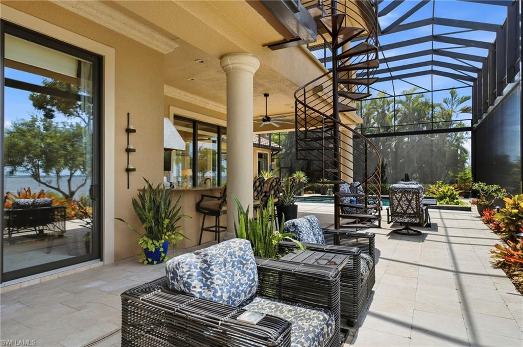 One side of this magnificent outdoor living space is thoughtfully designed for exceptional entertaining, featuring abundant lounge seating and bar seating at the outdoor kitchen. A striking spiral staircase leads gracefully to the upper balcony, while massive retractable electric awnings on both sides provide effortless shade and comfort, creating an extraordinary setting for enjoying the spectacular waterfront surroundings.