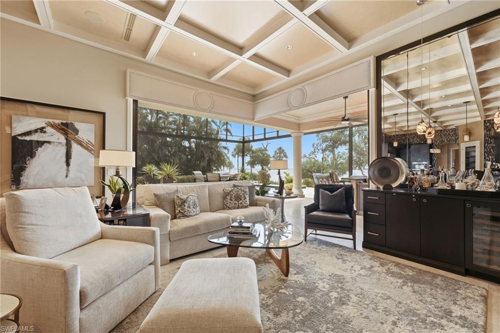 The grand living space is framed by breathtaking river views, an exquisite coffered ceiling, and a sophisticated bar area, with seamless access to an expansive outdoor living environment designed for effortless entertaining and refined relaxation.