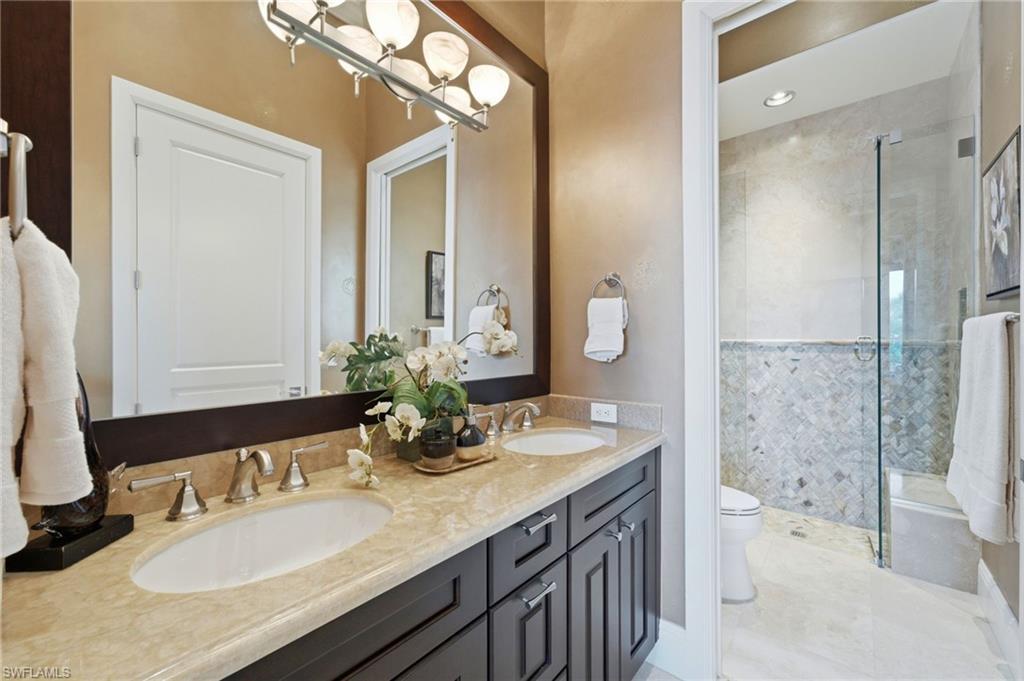 The second ensuite bath exudes luxury with dual marble-topped vanities, a spacious walk-in shower enclosed in seamless glass, elegant marble walls, and custom Listello detailing that adds a refined designer touch.