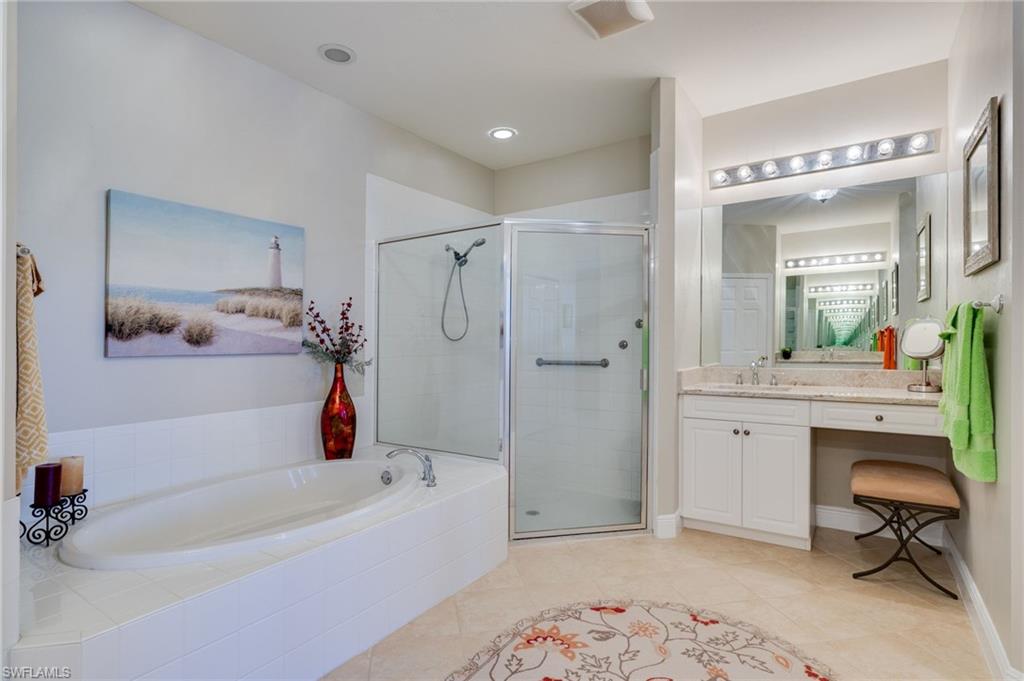 Built-in soaking tub, glass-enclosed shower, vanity with integrated seating area, recessed lighting, and tile flooring