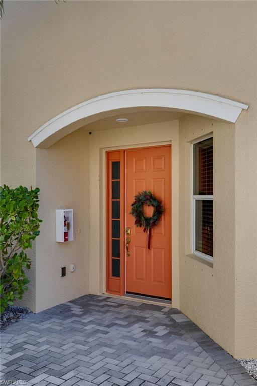 Recessed entry with an arched canopy, a vibrant orange front door, a sidelight, and herringbone paver flooring