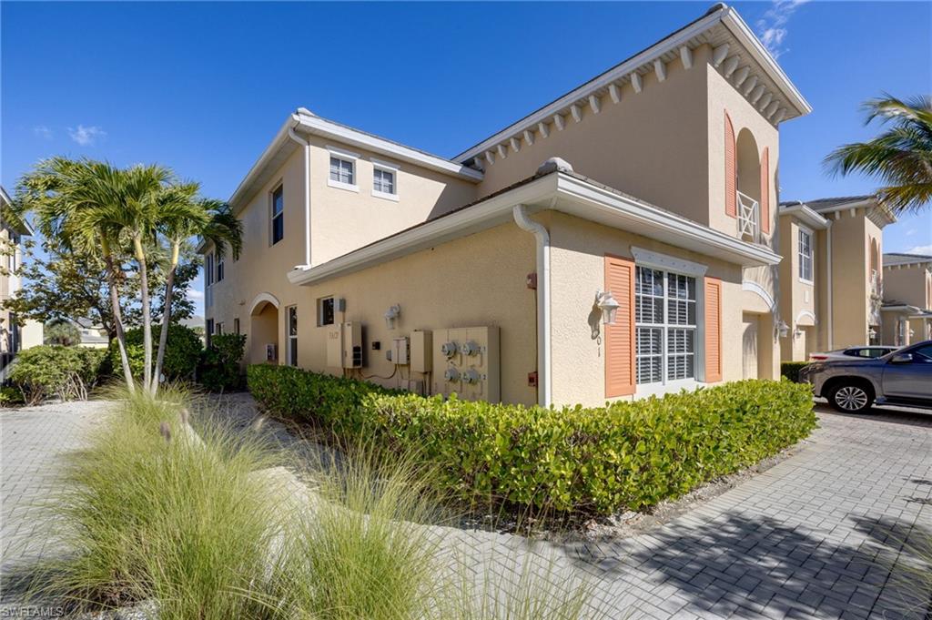 Stucco exterior with decorative window shutters, arched balcony, and a paver driveway