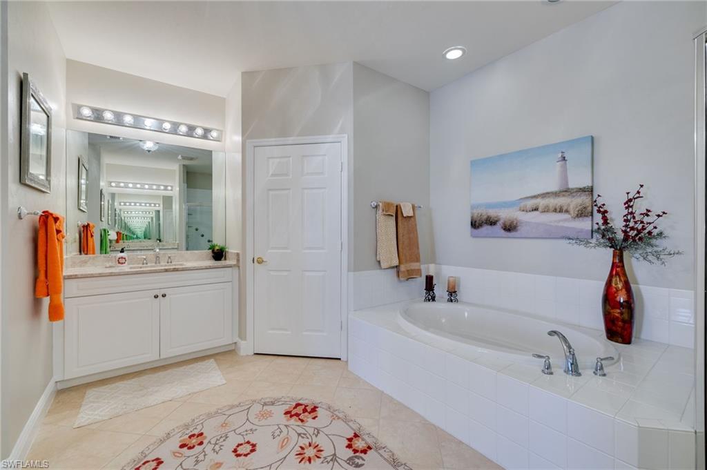 Bathroom featuring a built-in soaking tub, tiled surround, single vanity with a solid surface countertop, and large wall mirror with overhead lighting
