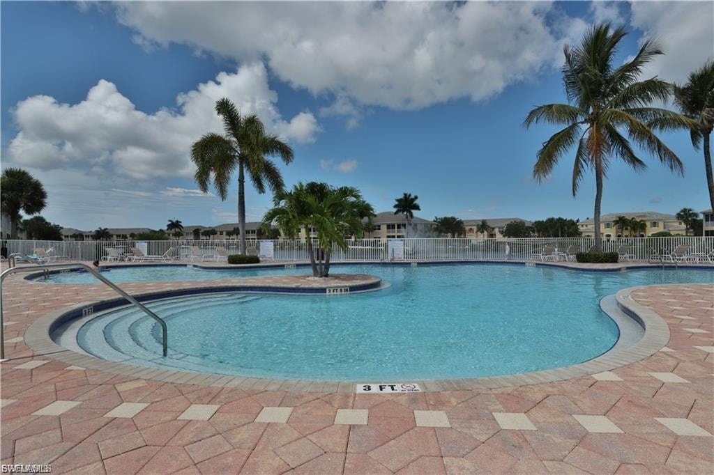 Pool with integrated steps, surrounded by patterned paver decking, a decorative island, and mature palm trees