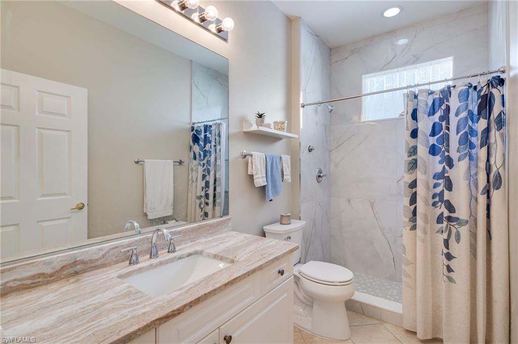 Vanity with an integrated sink and stone countertop, mirrored wall, white cabinetry, recessed lighting, and a walk-in shower with tile surround