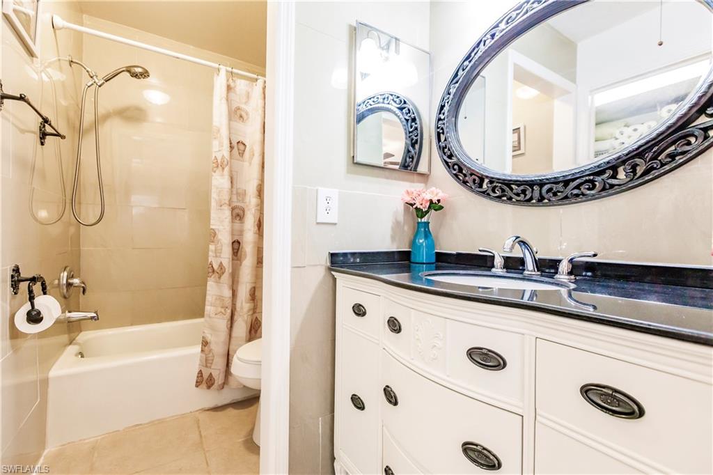 Bathroom featuring a white vanity with a dark countertop, an ornate oval mirror, and a built-in bathtub with shower