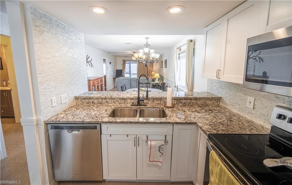 Kitchen featuring granite countertops, a stainless steel double basin sink with a matte black faucet, and white shaker-style cabinetry