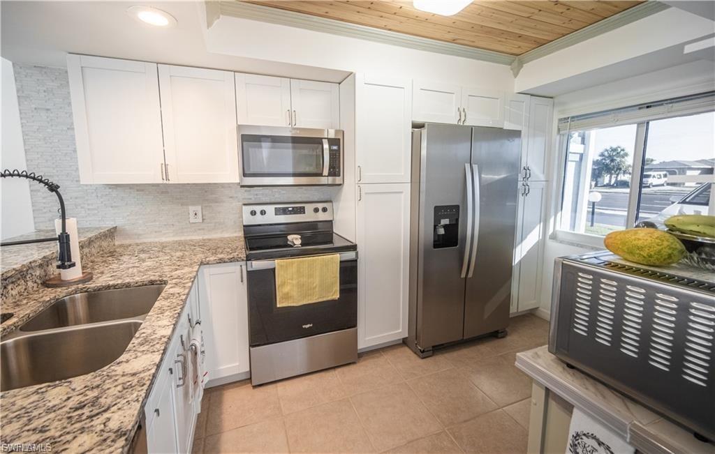 Kitchen with white shaker cabinetry, stainless steel appliances, granite countertops, a double basin sink, and a wood-panel ceiling