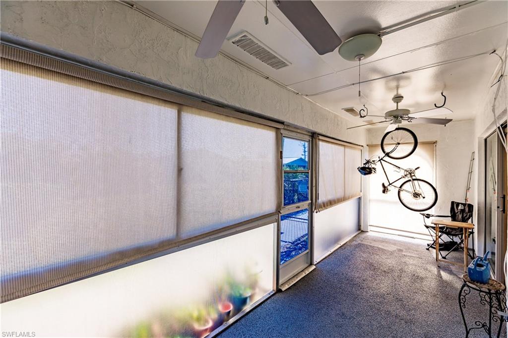 Enclosed patio space featuring textured walls, multiple ceiling fans, full-height window treatments, and a durable speckled floor finish