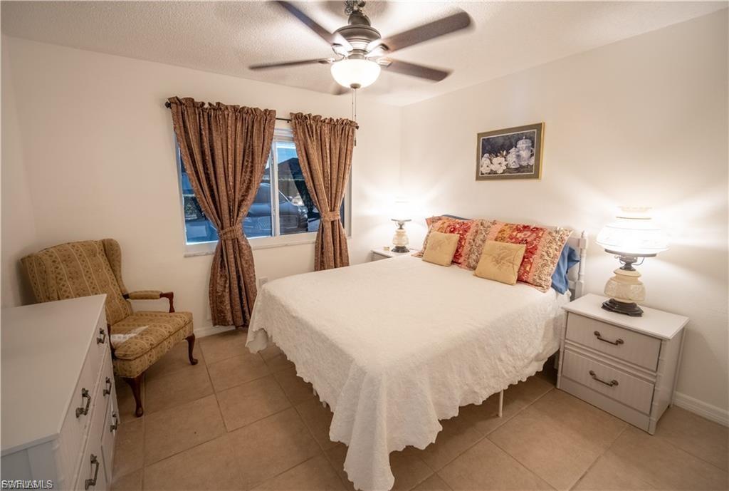 Bedroom featuring tile flooring, a ceiling fan with integrated lighting, and a window with custom drapery