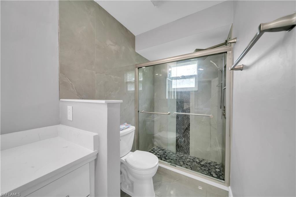 Modern bathroom featuring a sliding glass shower door, stone pebble shower floor, and large format wall tiling