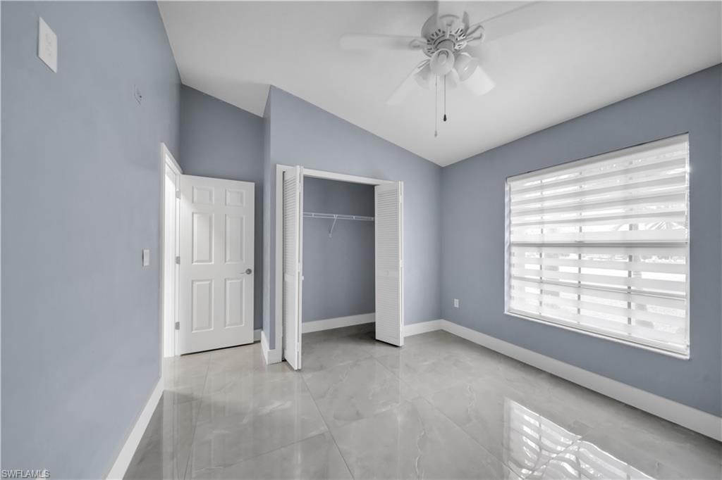 Vaulted ceilings, a ceiling fan with integrated lighting, a spacious window with blinds, bi-fold closet doors, and large format tile flooring
