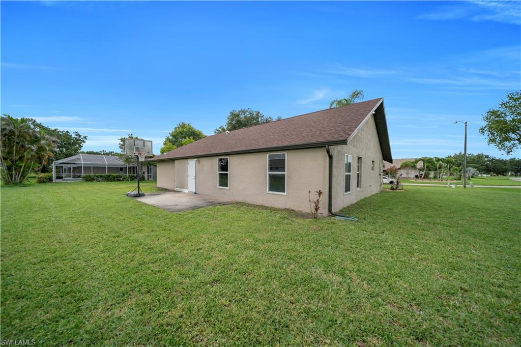 Expansive green lawn, stucco exterior, asphalt shingle roof, multiple windows, and a concrete patio