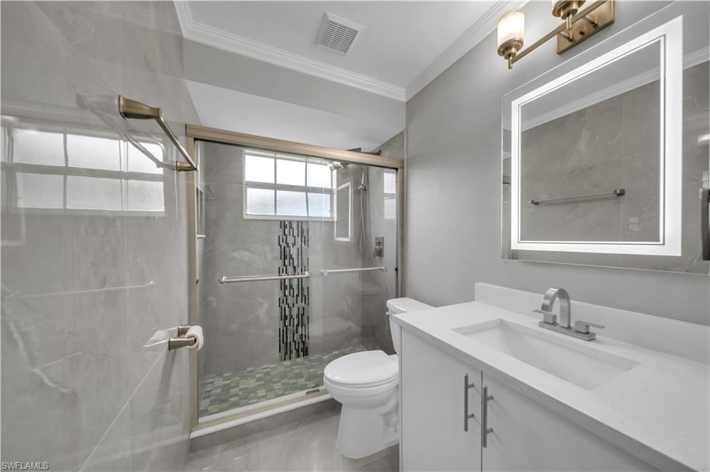 Sleek vanity with integrated sink, illuminated mirror, walk-in shower with sliding glass door, and mosaic tile accents