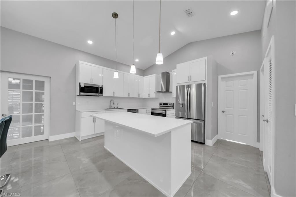 Open-concept kitchen featuring a center island, white cabinetry, stainless steel appliances, and vaulted ceilings