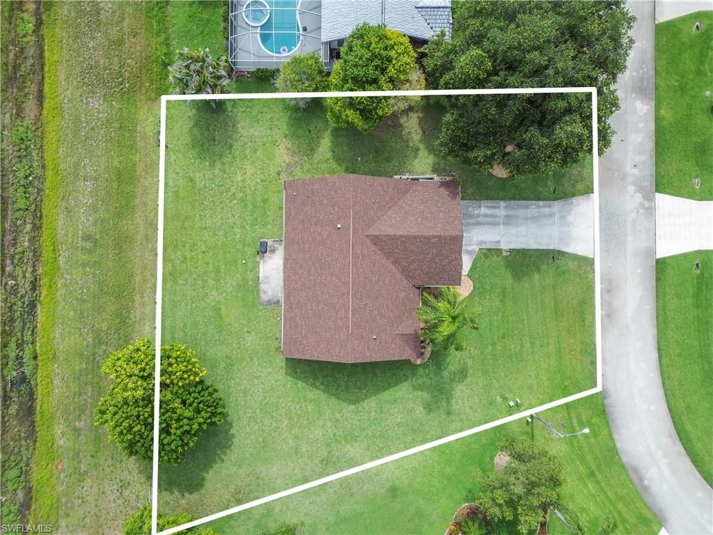 Expansive lot featuring a well-proportioned single-story residence with a brown composite roof, situated on manicured grounds with mature shade trees and lush green lawn