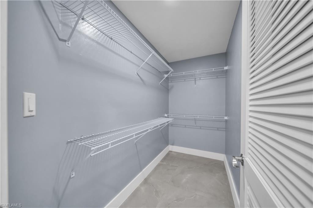 Walk-in closet featuring wire shelving, L-shaped shelving, gray wall paint, white trim, and a louvered door
