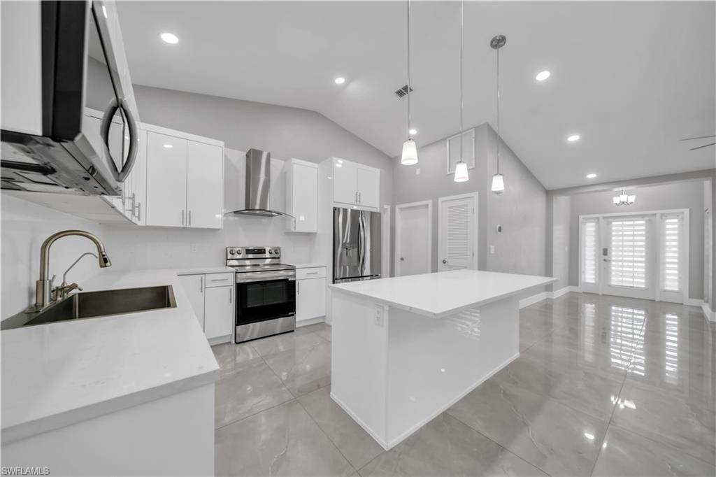 Vaulted ceiling, recessed lighting, white gloss cabinetry, stainless steel appliances, and a central kitchen island