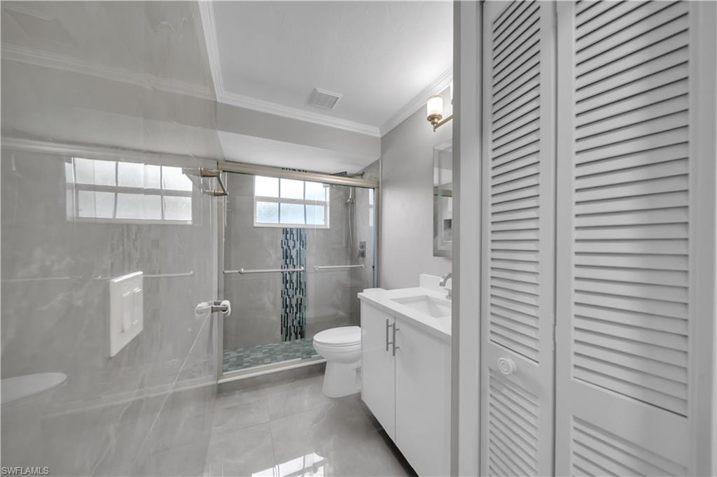 Glass-enclosed shower with decorative tile accent, white vanity with integrated sink, modern overhead lighting, and louvered bifold doors